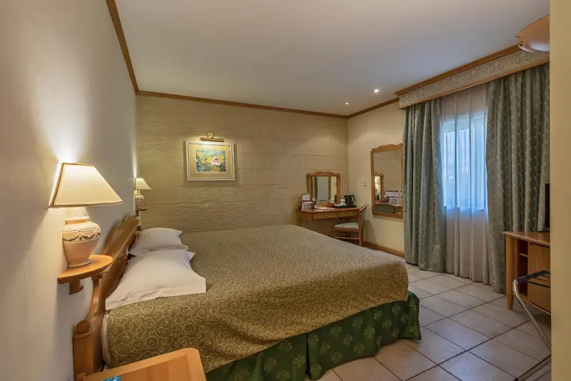 Une chambre lumineuse avec un lit double et un bureau près de la fenêtre.