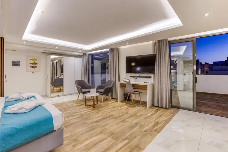 Une chambre spacieuse avec un lit fait et un coin salon donnant sur une terrasse.