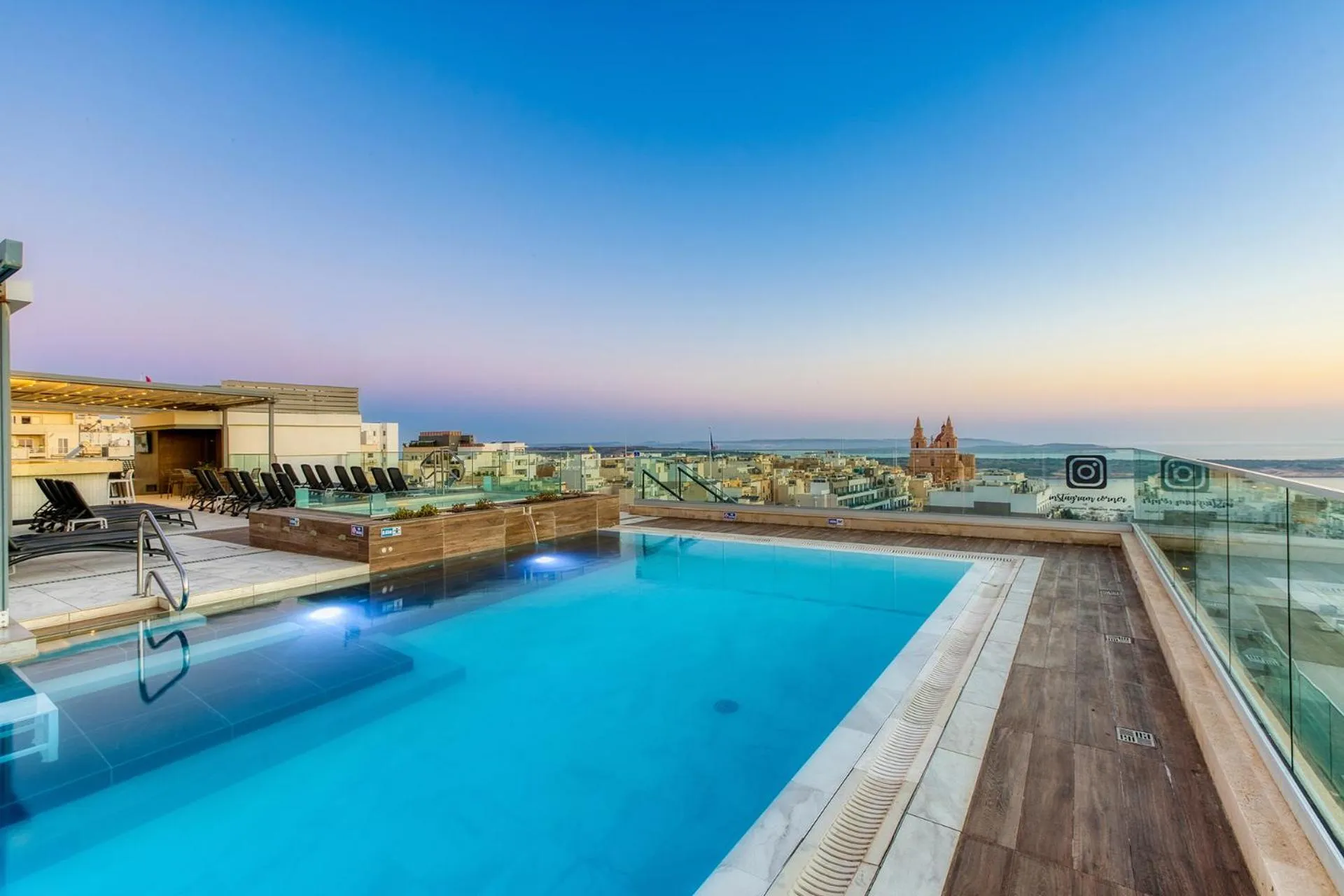 Piscine sur toit-terrasse avec vue sur la ville au crépuscule.