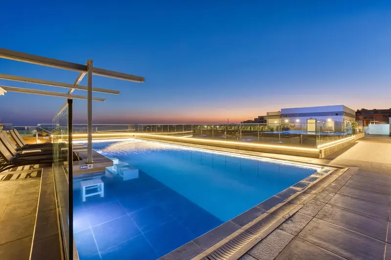 Piscine illuminée sur un toit-terrasse avec vue sur le ciel crépusculaire.