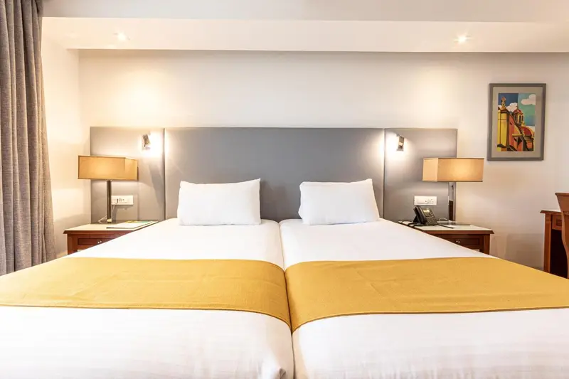 Une chambre lumineuse avec deux lits simples et des lampes de chevet.