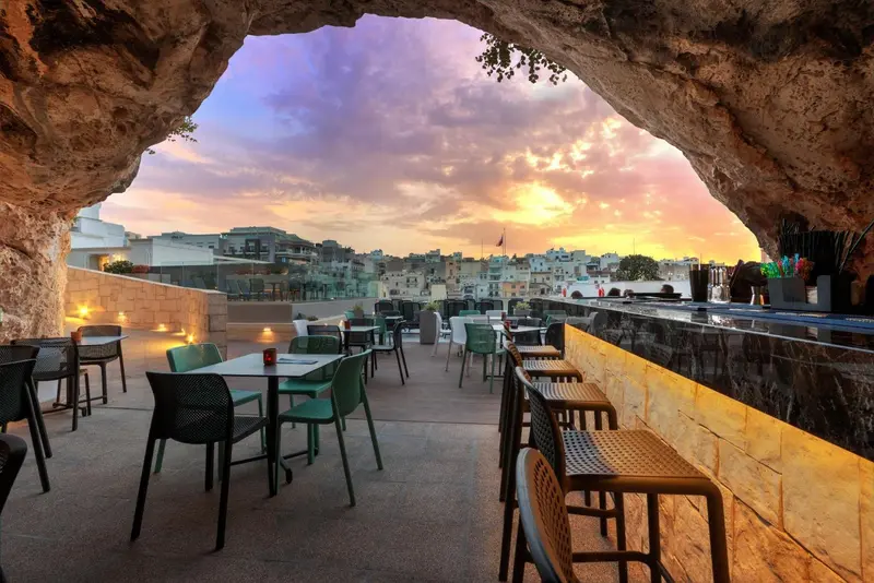 Terrasse avec tables et chaises donnant sur un paysage urbain au coucher du soleil.