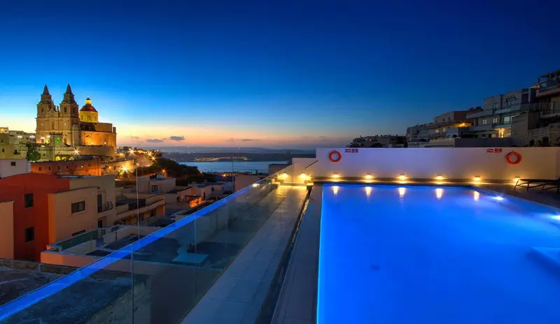 Une piscine illuminée surplombe une ville côtière au crépuscule.