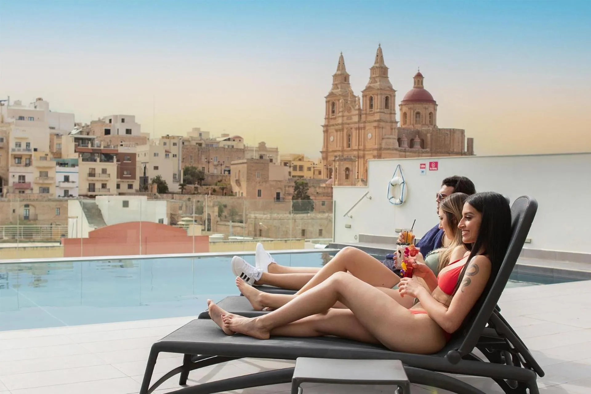 Des personnes se détendent sur des transats au bord d'une piscine avec une vue sur une ville.