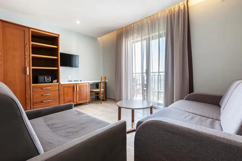 Espace de séjour lumineux avec canapé, bureau et accès à un balcon.