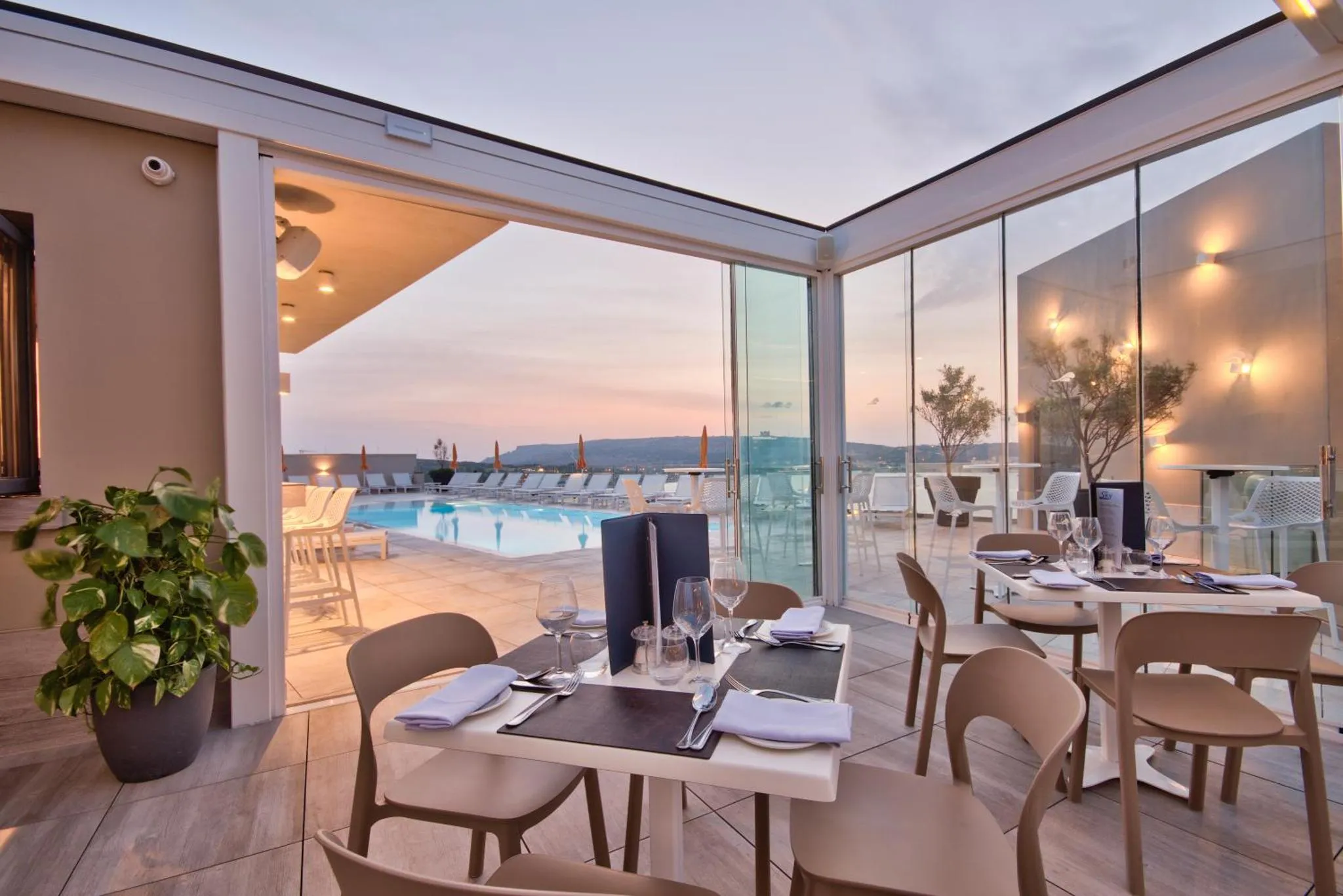 Tables dressées en terrasse avec vue sur une piscine et la mer au loin.