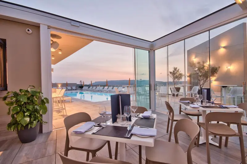 Tables dressées en terrasse avec vue sur une piscine et la mer au loin.