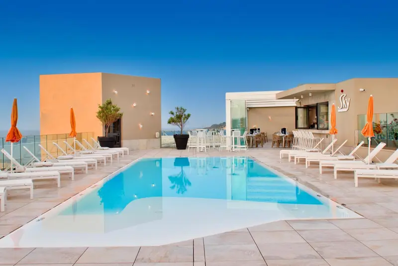 Terrasse avec piscine et chaises longues sous un ciel bleu.
