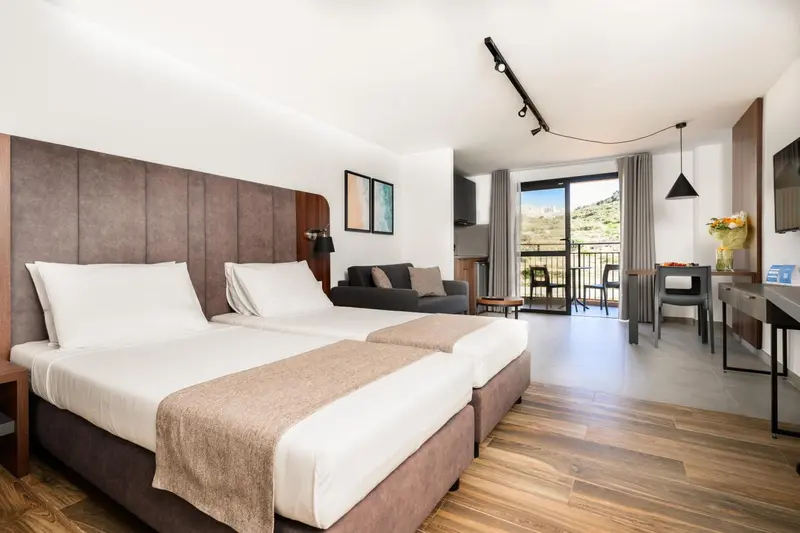 Une chambre avec un grand lit et un espace salon donnant sur une terrasse.