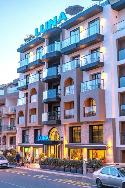 Façade d'un bâtiment moderne avec des balcons illuminés et une enseigne lumineuse.