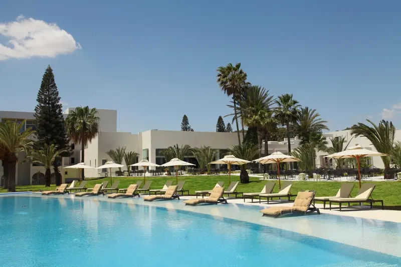 Transats alignés au bord d'une piscine turquoise dans un jardin tropical.