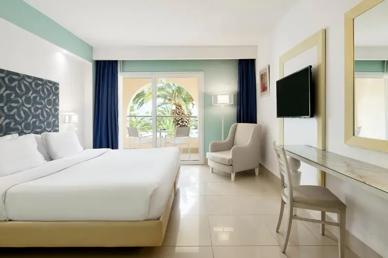 Une chambre lumineuse avec un lit double et un coin salon donnant sur une terrasse.