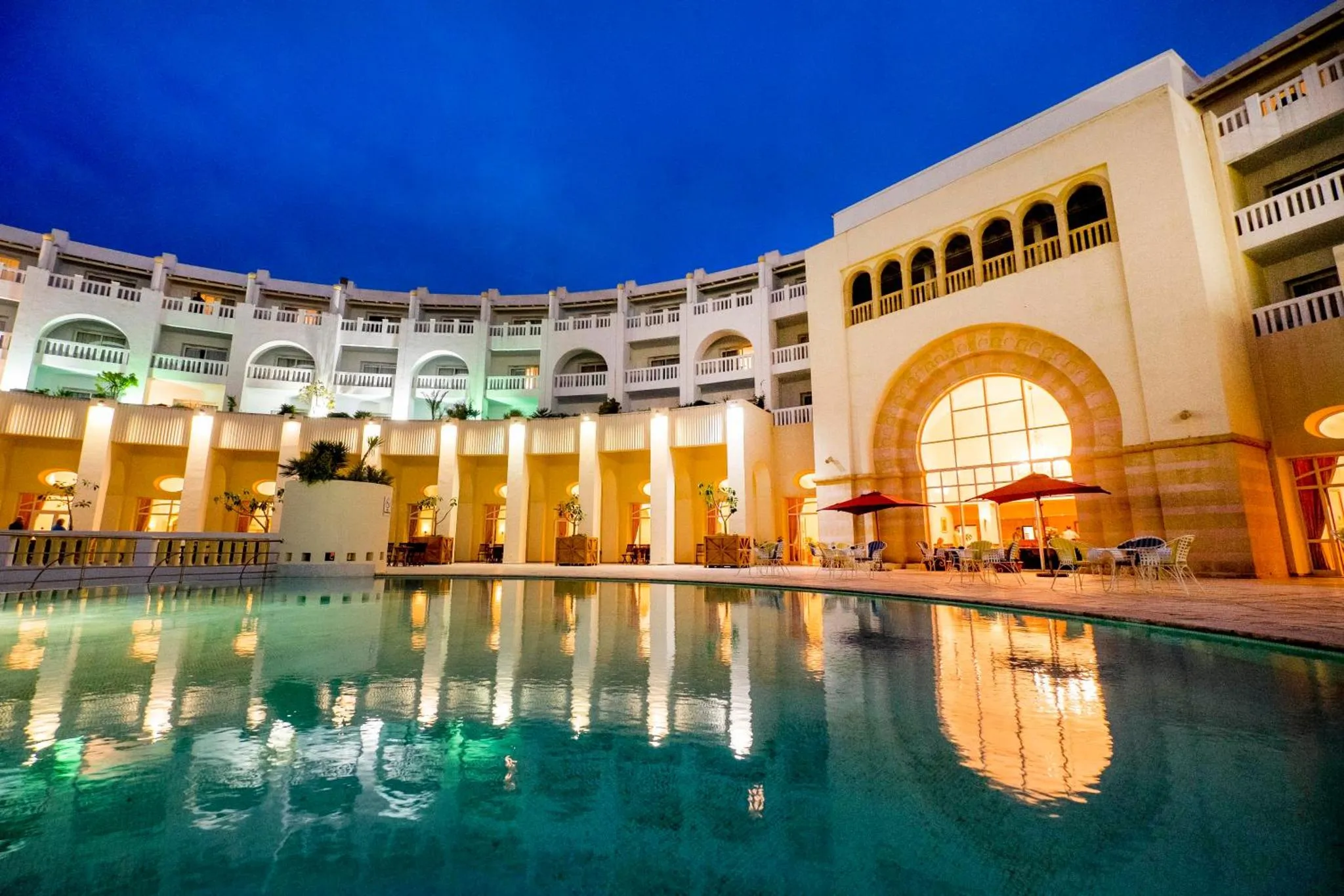 Bâtiment clair illuminé reflété dans une piscine calme au crépuscule.