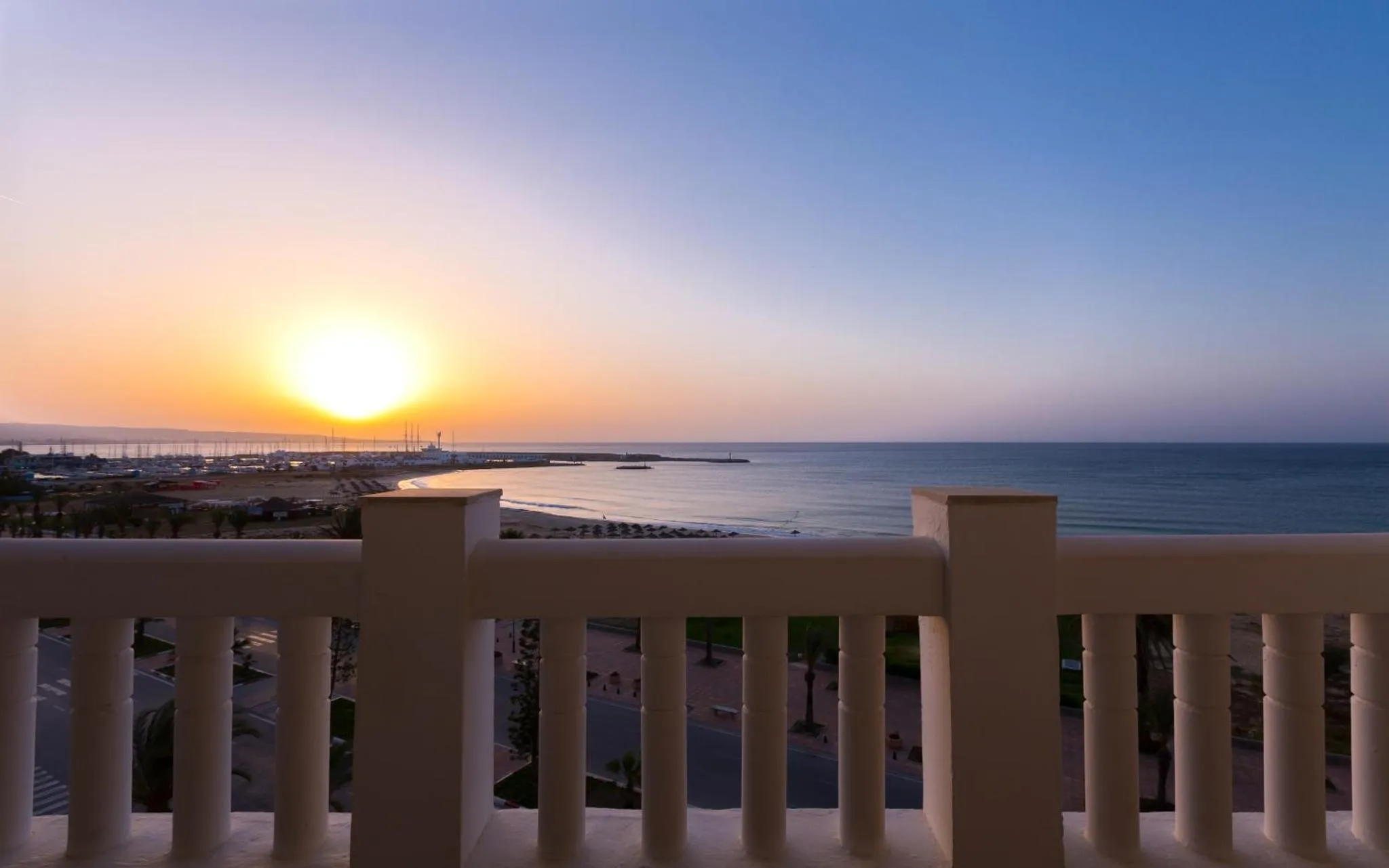 Vue sur la mer au coucher du soleil depuis un balcon blanc.