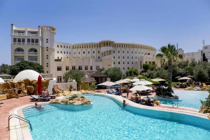 Baignade dans une piscine ensoleillée devant un bâtiment blanc.