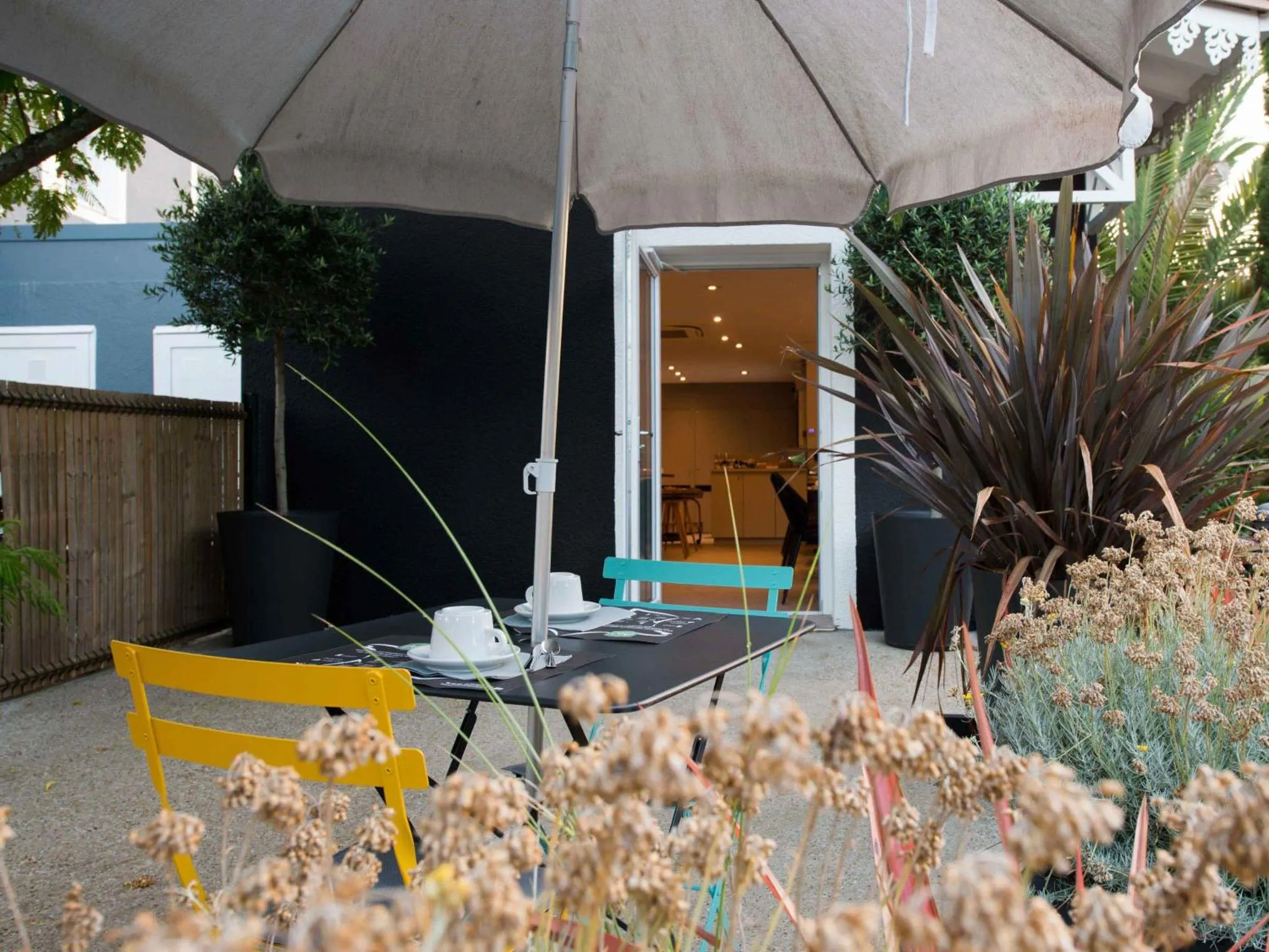 Une table est dressée sur une terrasse ombragée avec des chaises colorées.