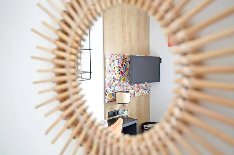 Une télévision murale est encadrée par une décoration en bois et surplombe une table de chevet avec une lampe.