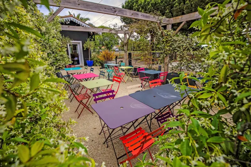 Terrasse ombragée avec tables et chaises colorées dans un jardin.