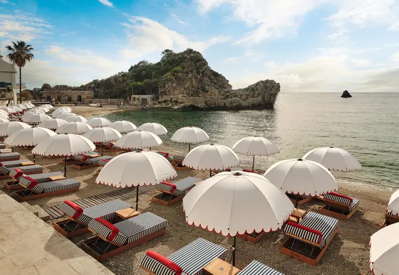 Transats rayés et parasols blancs sur une plage de sable fin.