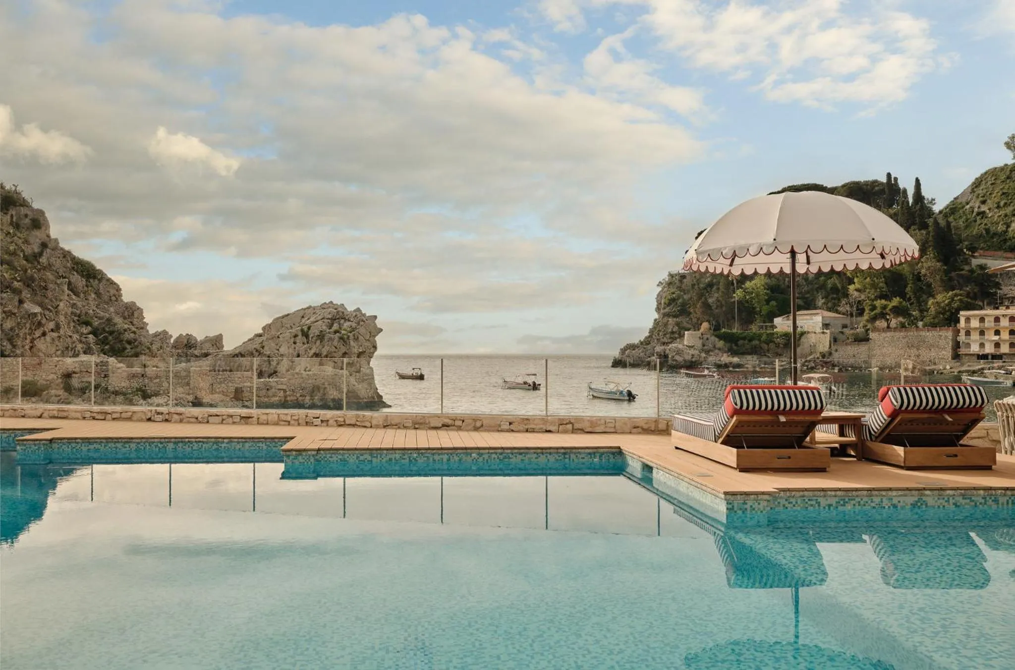 Transats et parasol rayés au bord d'une piscine à débordement avec vue sur la mer.