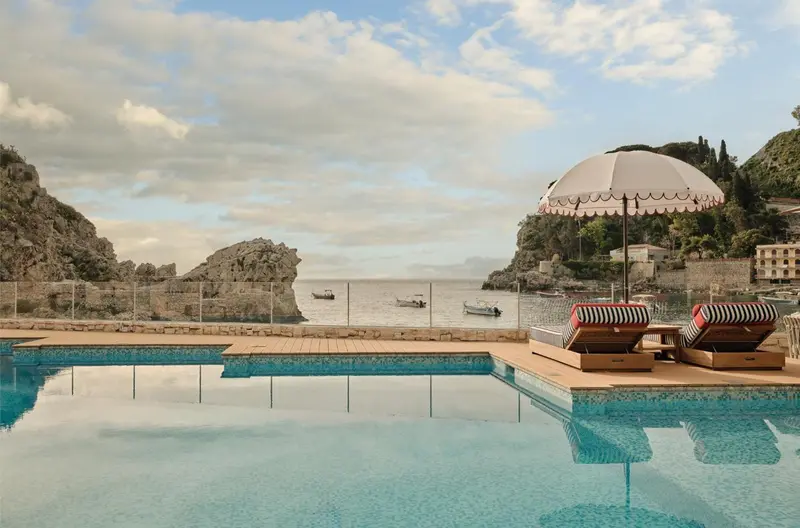 Transats et parasol rayés au bord d'une piscine à débordement avec vue sur la mer.
