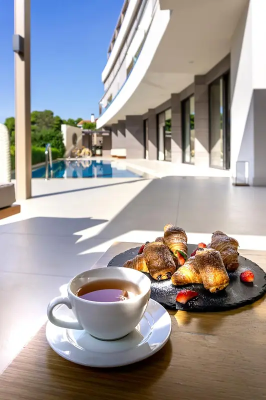 Une tasse de café et des pâtisseries sont présentées sur une table ensoleillée près d'une piscine.