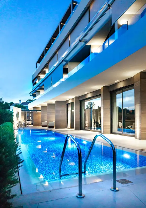 Piscine rectangulaire devant un bâtiment moderne avec de grandes baies vitrées.