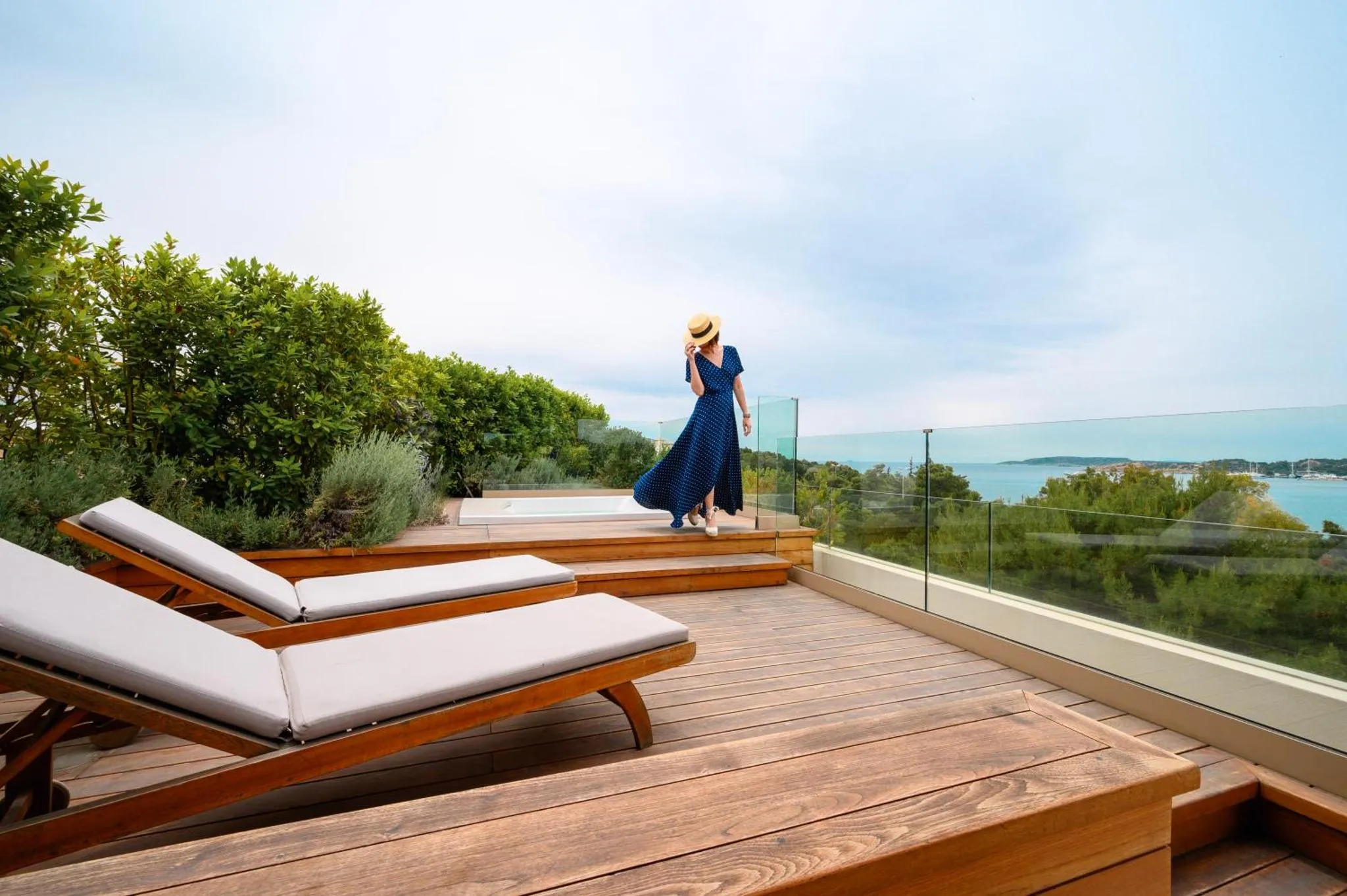 Une femme se promène sur une terrasse en bois avec vue sur la mer.
