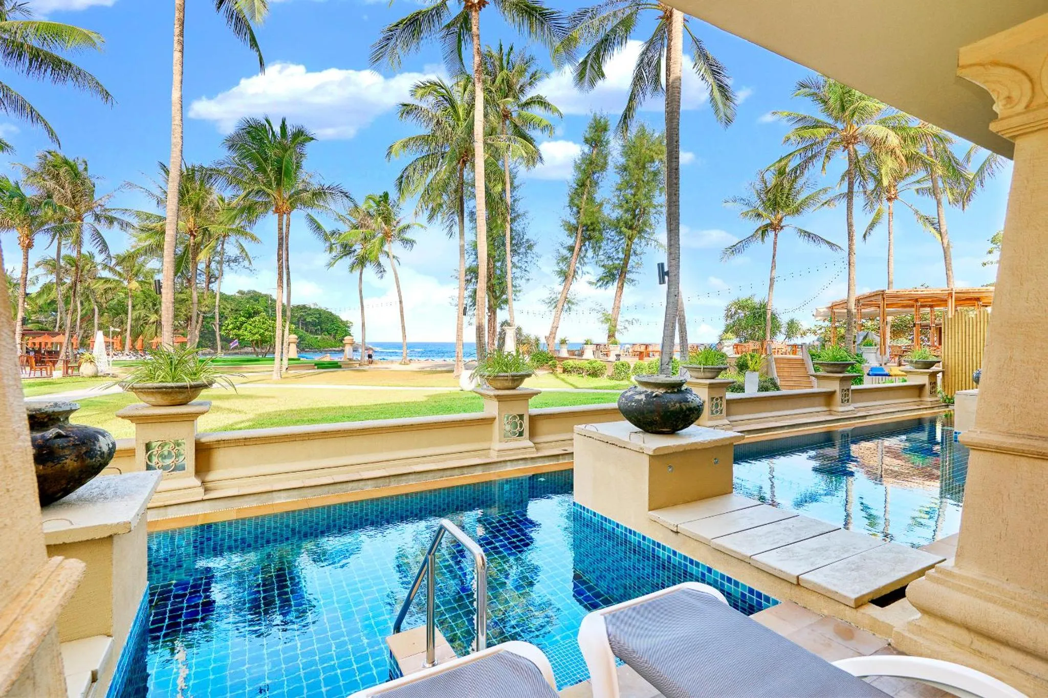 Une piscine turquoise avec des transats offre une vue sur la mer et la végétation tropicale.