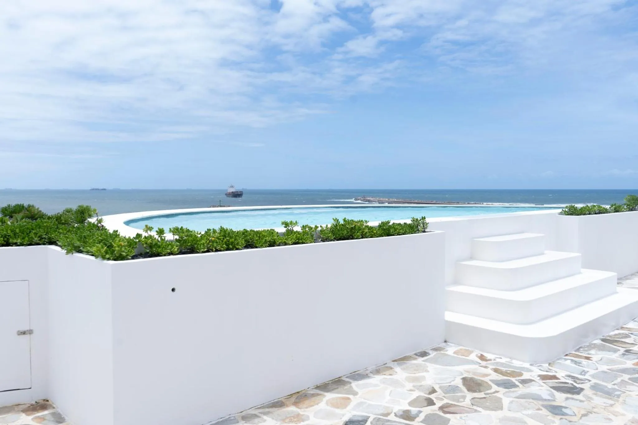 Piscine à débordement blanche surplombant la mer et le ciel bleu.