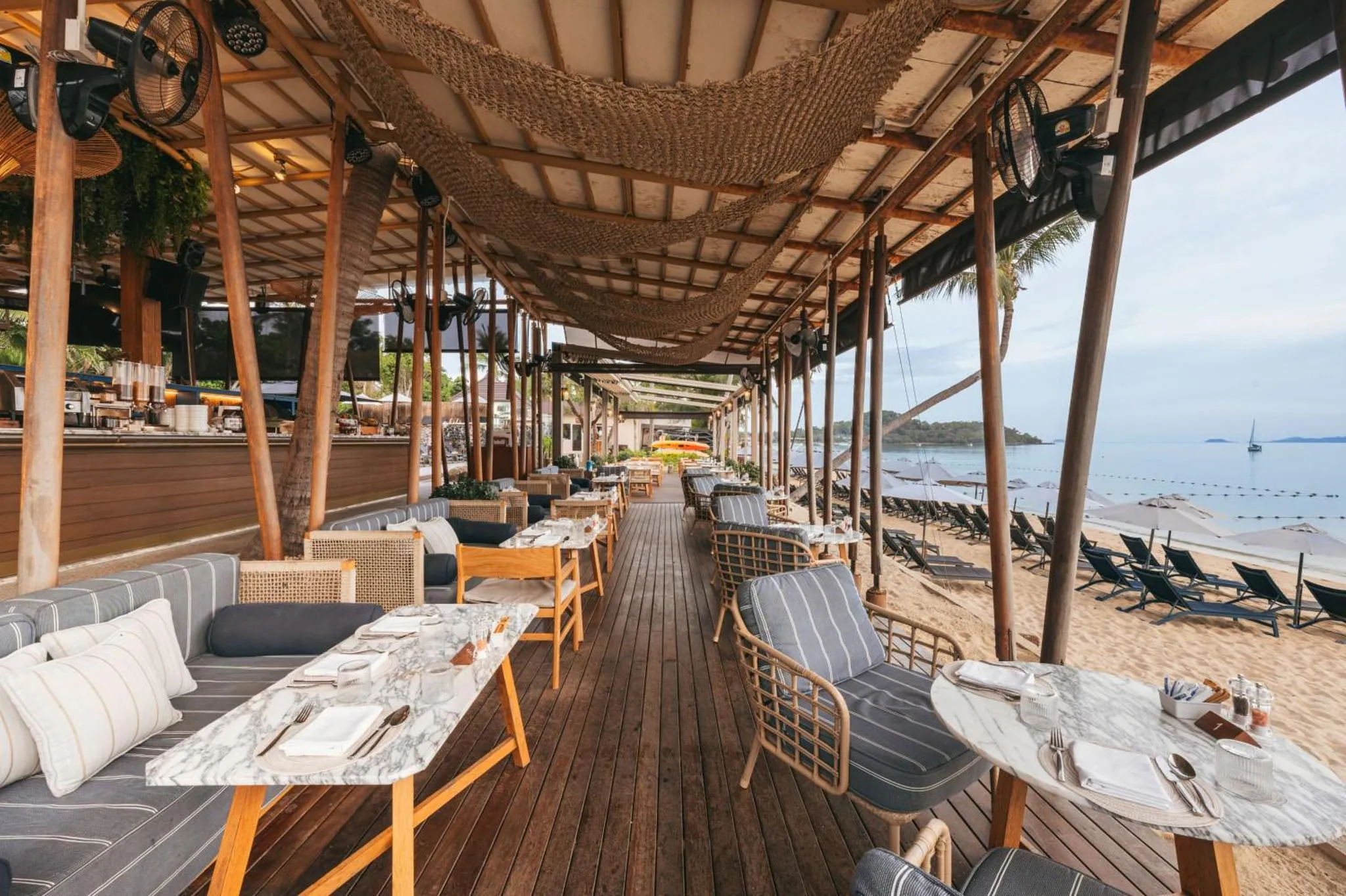 Terrasse de restaurant en bois avec tables et chaises face à la mer.
