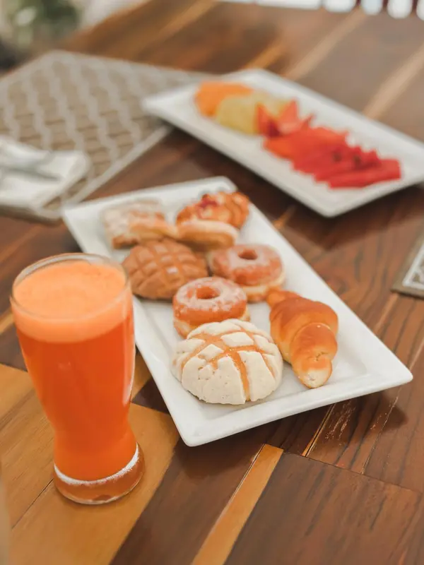 Une table en bois présente un petit-déjeuner avec des viennoiseries, des fruits et un jus d'orange.