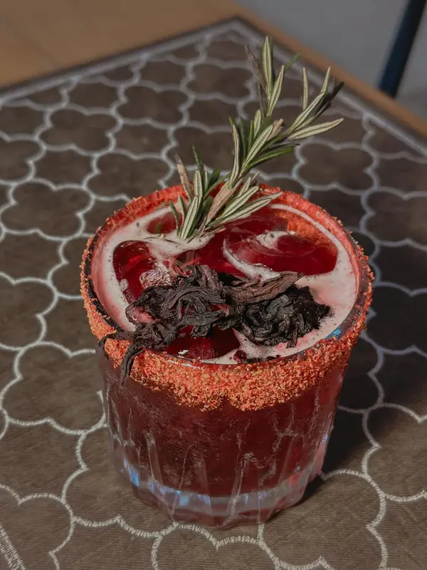 Un verre coloré garni d'une tranche d'agrumes et d'une branche de romarin est posé sur une table.