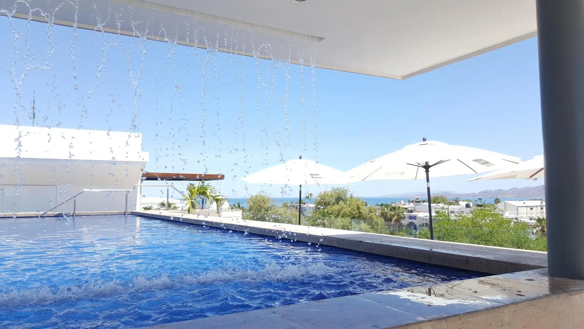 Une piscine à débordement offre une vue sur la mer et un paysage ensoleillé.