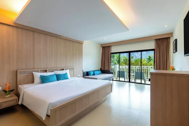 Une chambre lumineuse avec un grand lit et un espace salon donnant sur une terrasse.