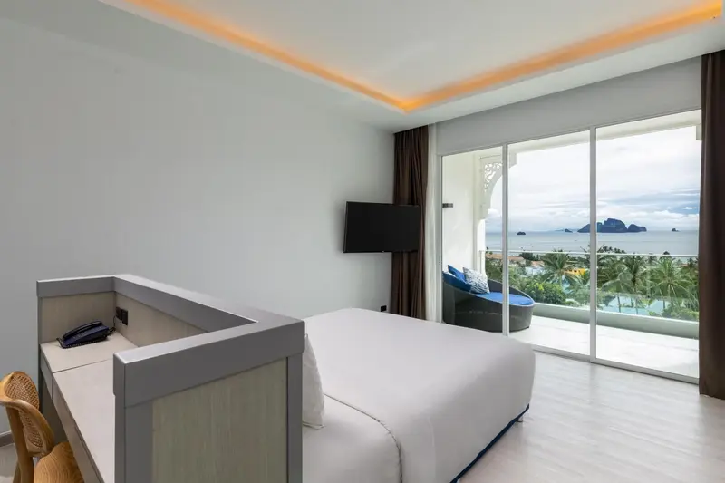 Chambre lumineuse avec un lit blanc et une vue sur la mer.
