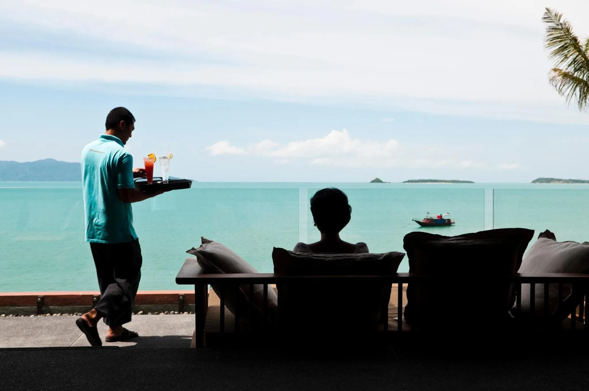Un serveur porte des boissons sur une terrasse avec vue sur la mer.
