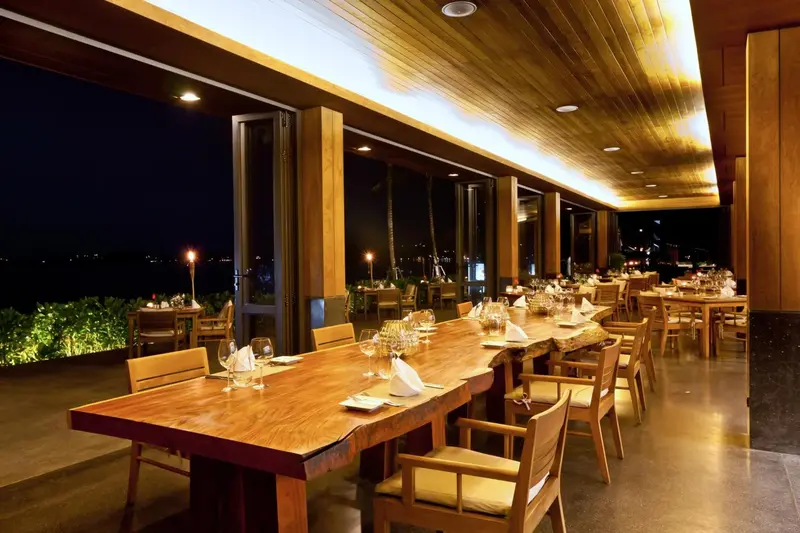 Une salle à manger lumineuse avec des tables dressées face à une vue nocturne.