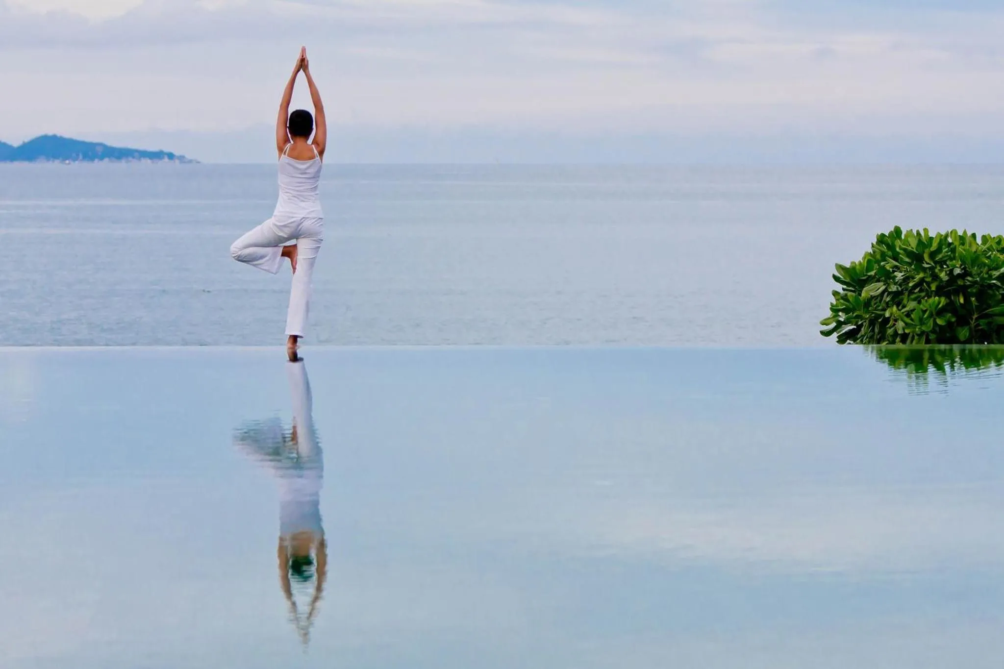 Une personne pratique le yoga au bord d'une piscine à débordement avec vue sur la mer.
