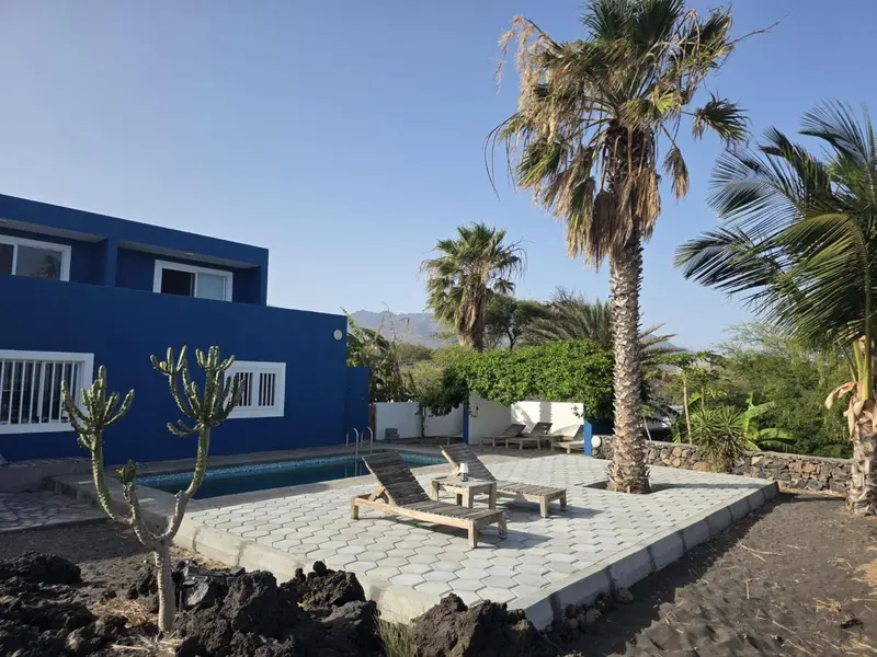 Terrasse ensoleillée avec chaises longues près d'une piscine et de bâtiments bleus.