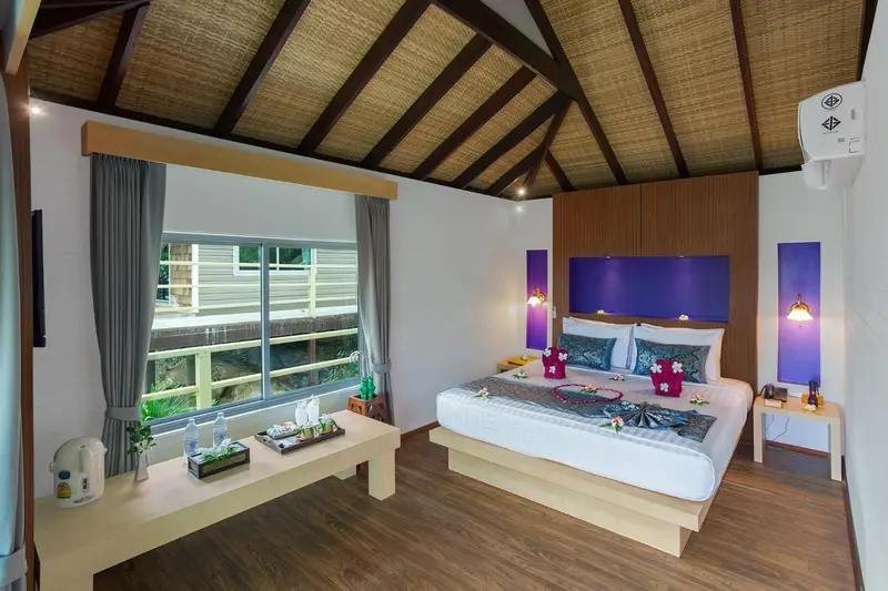 Chambre lumineuse avec un lit décoré de fleurs et une fenêtre donnant sur la végétation.