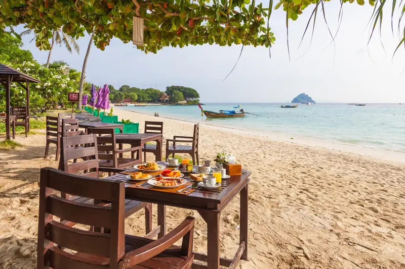 Une table est dressée sur le sable avec un petit-déjeuner face à la mer.