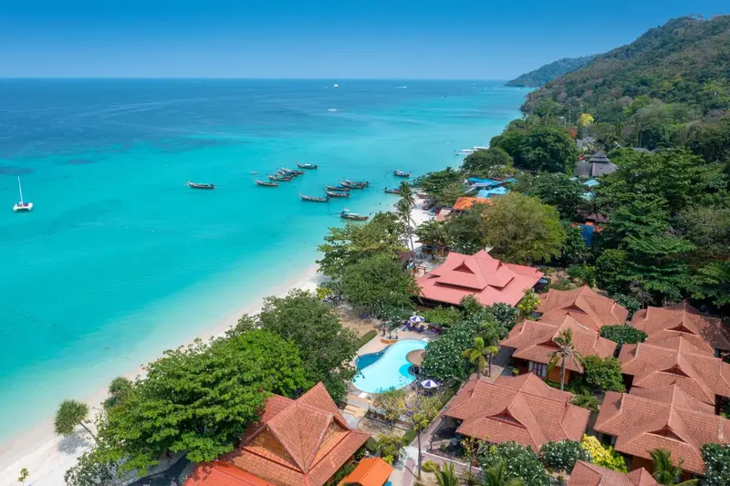 Vue aérienne d'une plage bordée de bâtiments et de végétation luxuriante.