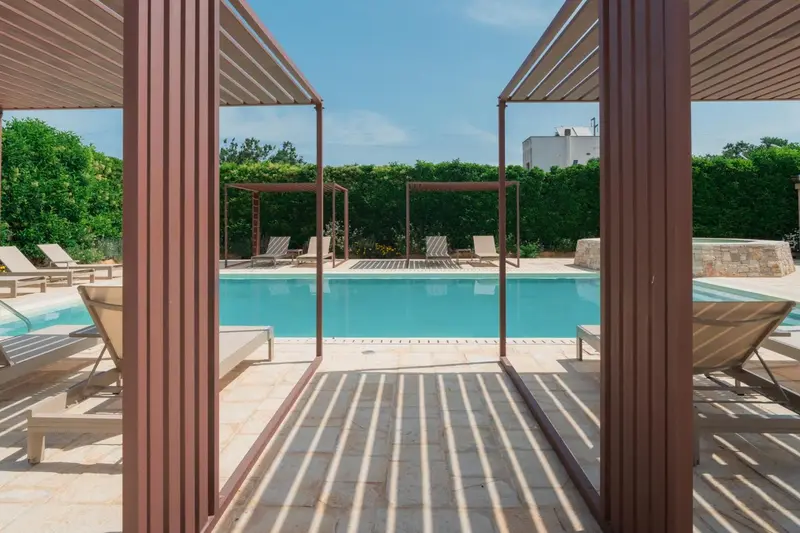 Transats alignés au bord d'une piscine rectangulaire sous une pergola.