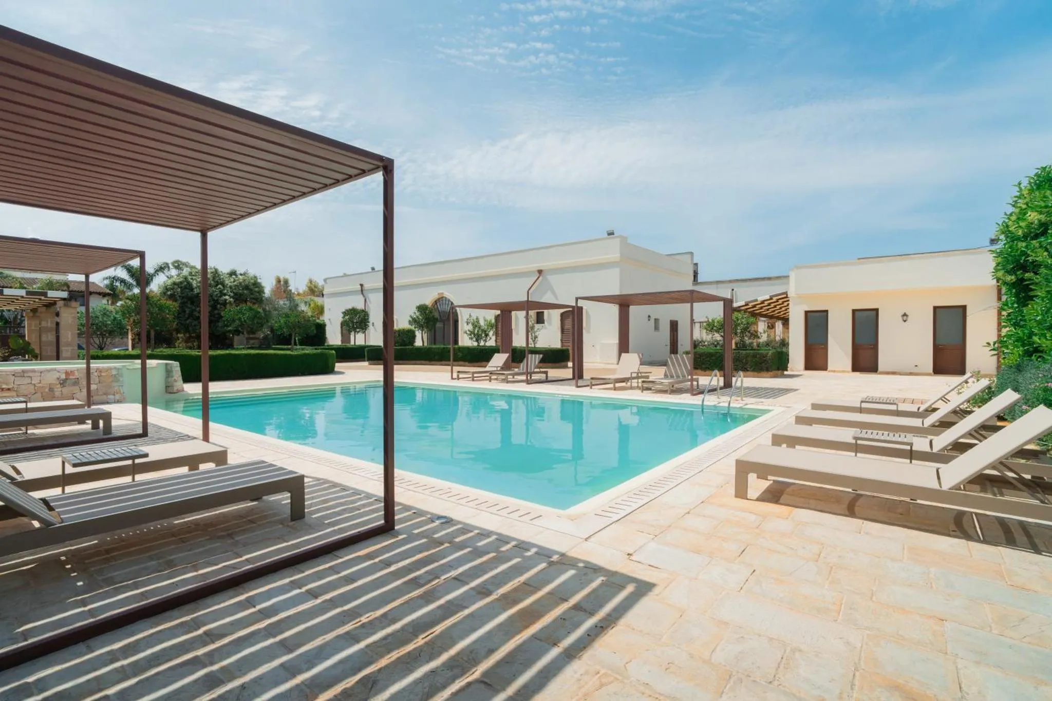 Transats et parasols bordent une piscine rectangulaire dans un espace extérieur ensoleillé.