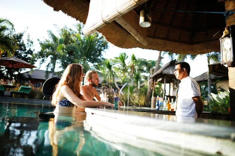 Des clients discutent avec le barman au comptoir d'un bar de piscine.