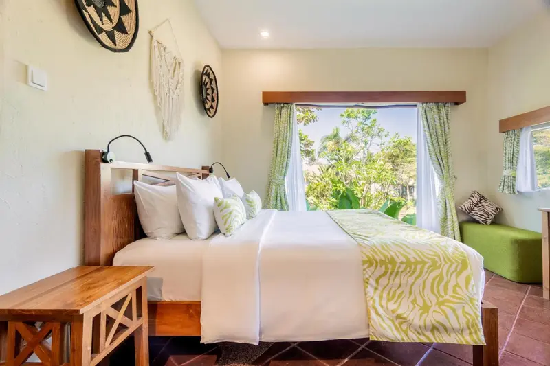 Une chambre lumineuse avec un grand lit et vue sur la végétation.