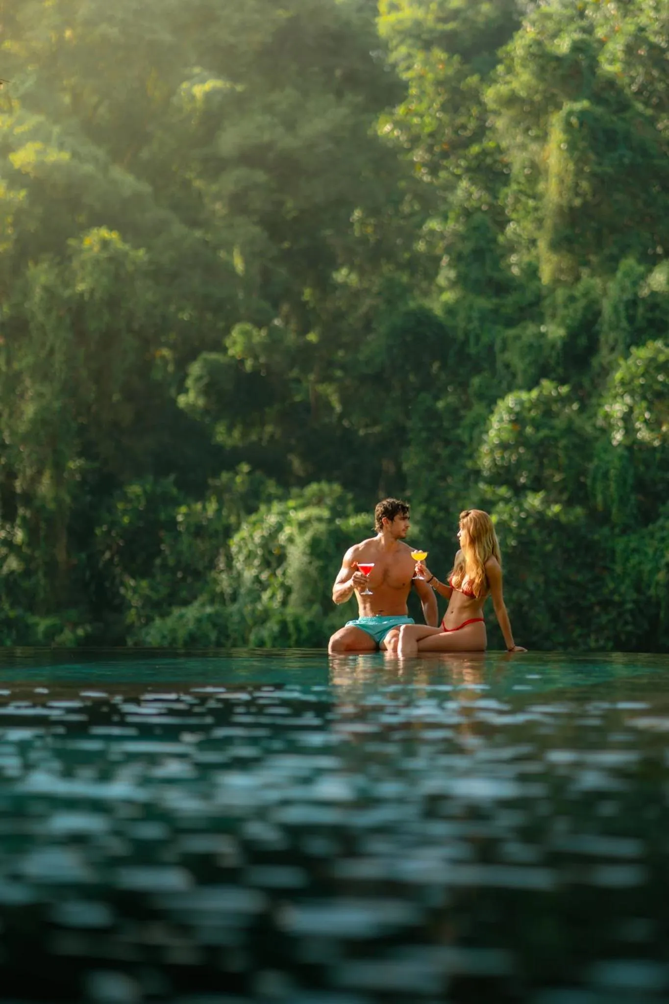 Un couple se détend dans une piscine turquoise bordée de végétation luxuriante.