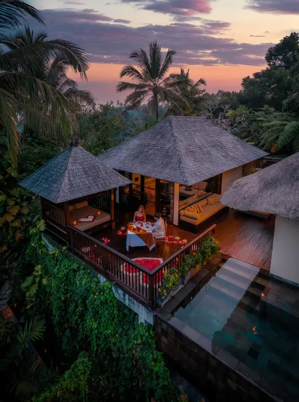 Une table est dressée sur une terrasse en bois avec vue sur une piscine et une végétation luxuriante.