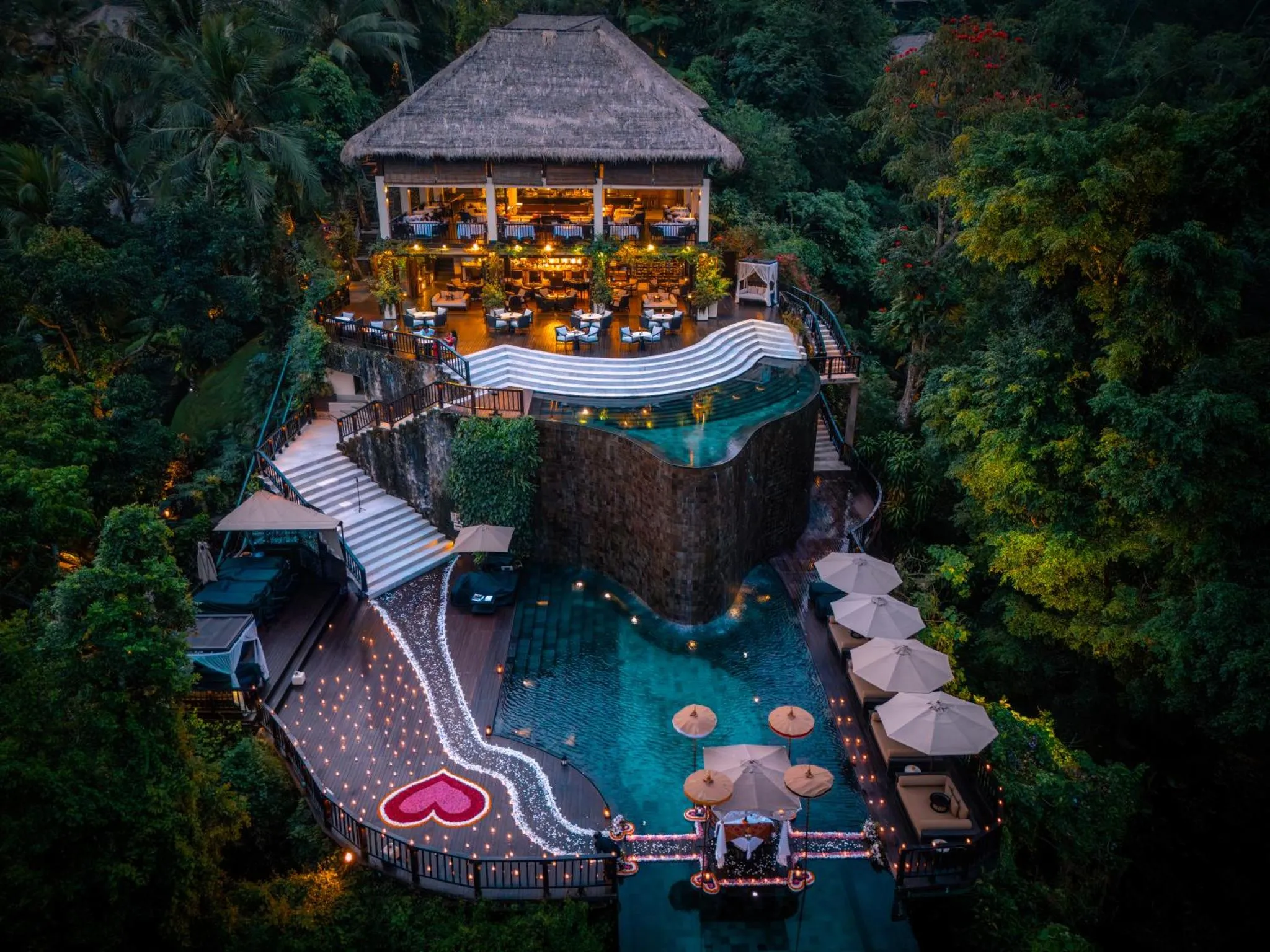 Vue aérienne d'un restaurant avec piscine illuminée et végétation luxuriante.